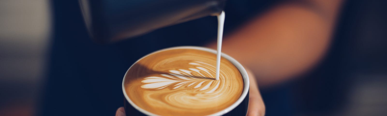 A close-up of a barista pouring milk to create a leaf pattern on an espresso base.