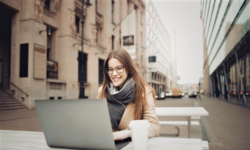 Mulher trabalha em um computador no centro da cidade, sorrindo e tomando um café