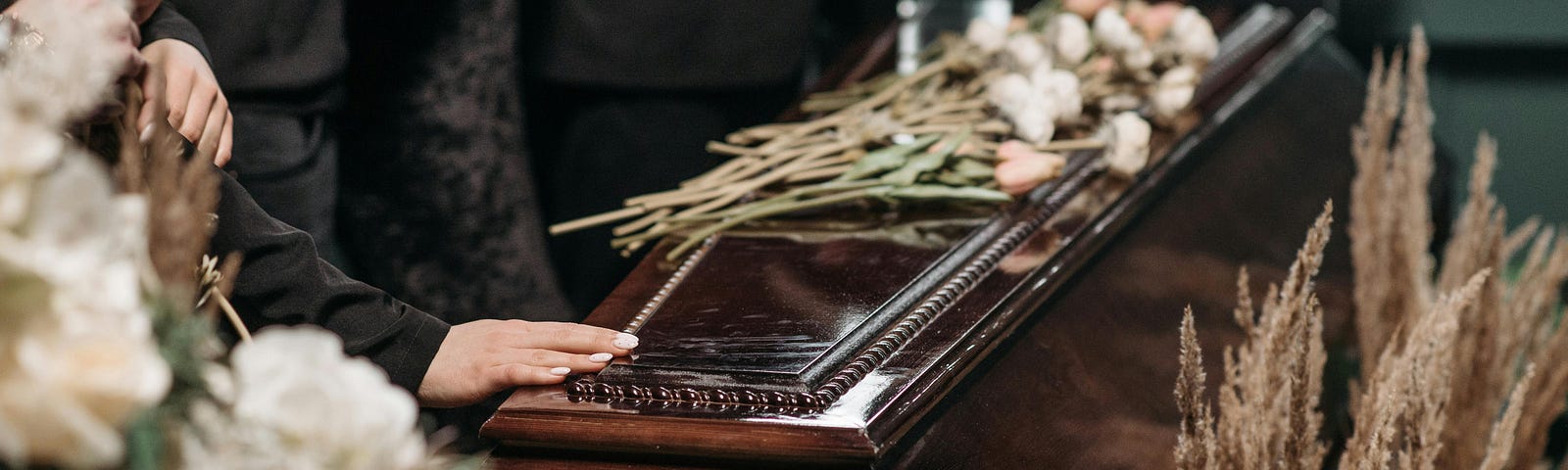 A wooden casket surrounded by flowers and people dressed in black.