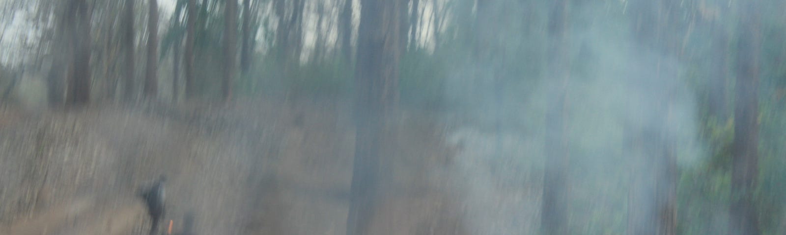 A blurred image of burning pyre and smoke. Some blurred human figures in the background.