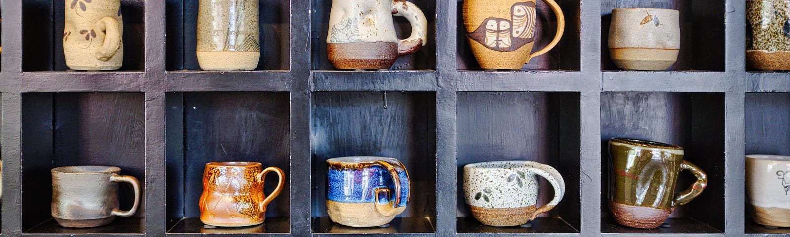 A lot different types of mugs, presented in a cupboard together