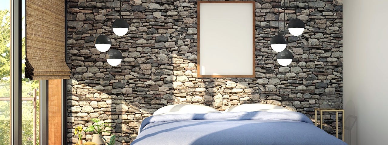 A bedroom with the head if the bed against a stone feature wsll and the bed swathed in sunshine.