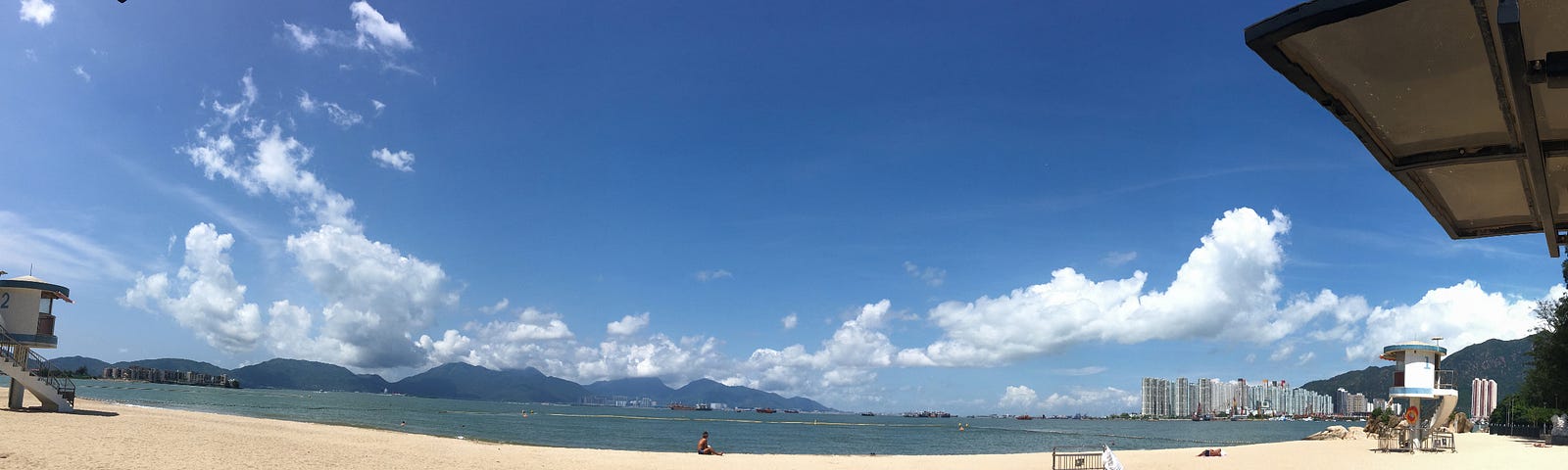 A panorama view of a beach of sunny blue sky with super white clouds on the yellow sand.