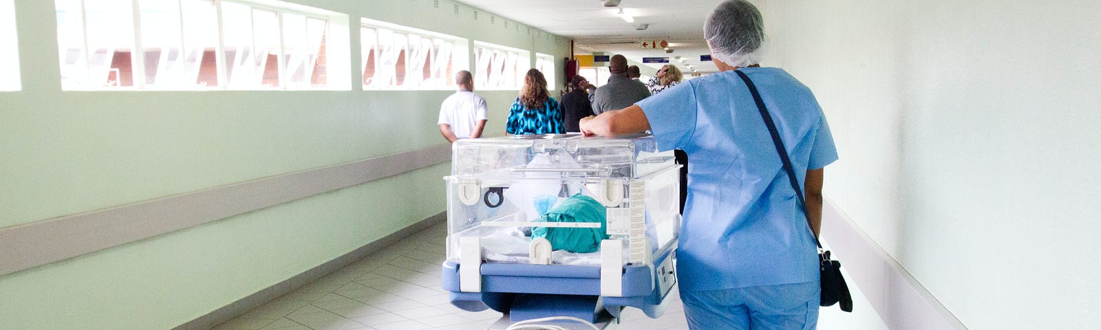 A nurse pushes an incubator in a hospital hallway.