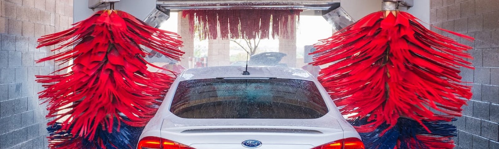 A car going through a car wash. White car with red rollers.