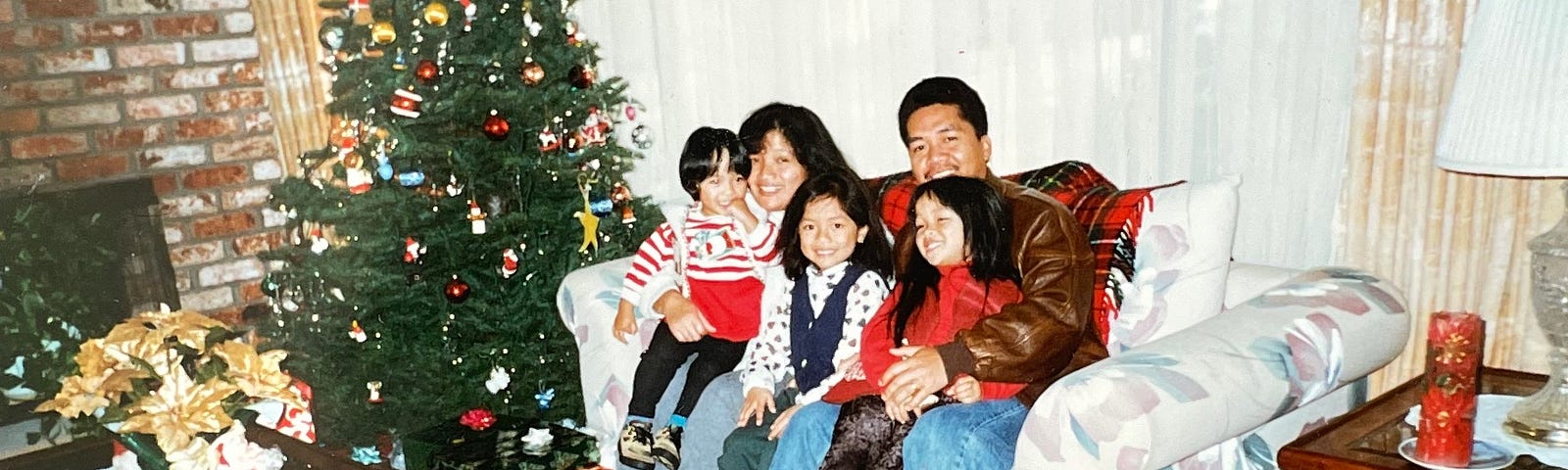 Family of 5 sitting at a couch by a Christmas tree