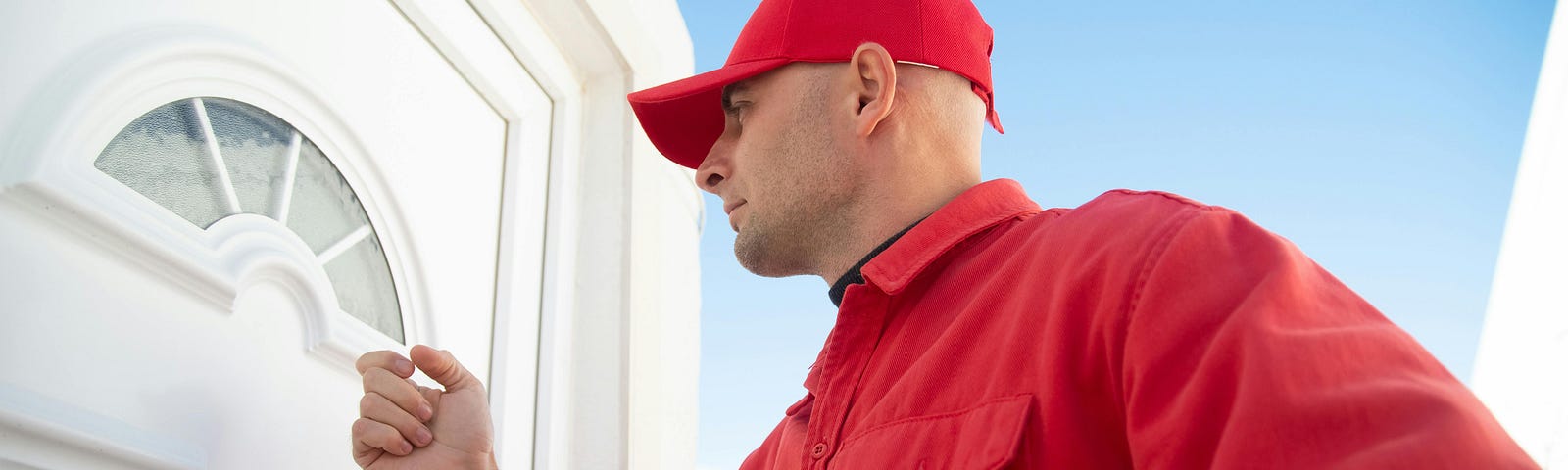 Man in red shirt and hat holding clipboard and knocking on home door