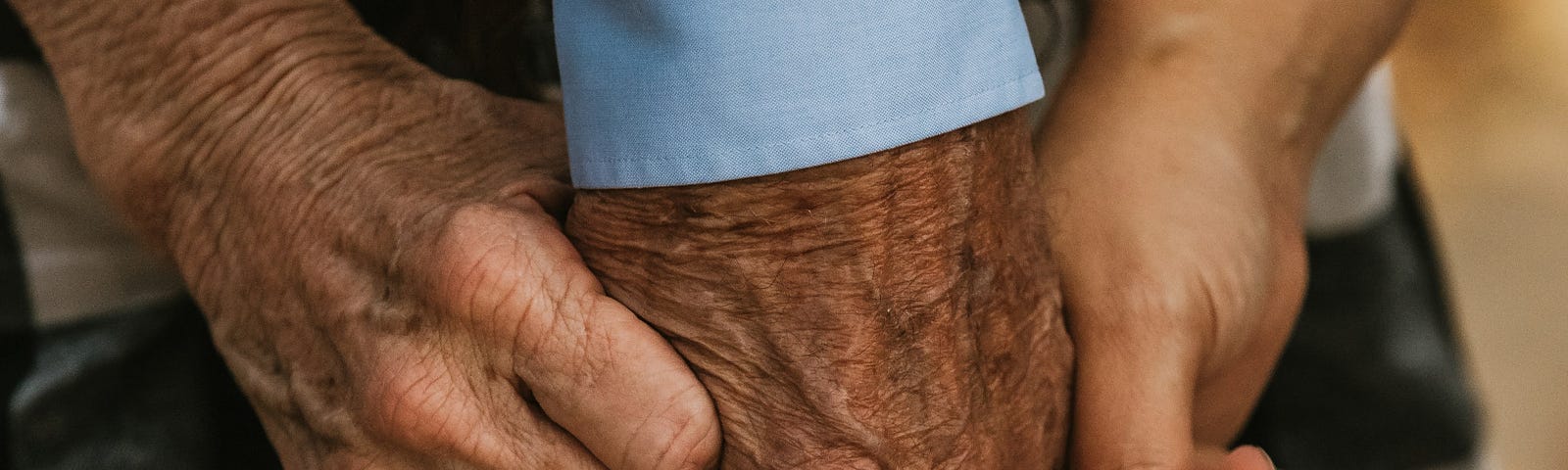 Photo shows hands of different sizes holding onto the fingers of an older man.