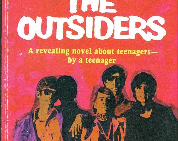 Book cover for SE Hinton’s The Outsiders, featuring a group of young men against a red and pink background.