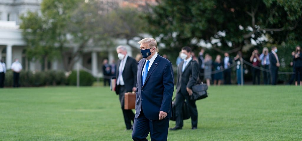 Trump walking alone on the White House grass, wearing a mask. Two aides walk in the distance.