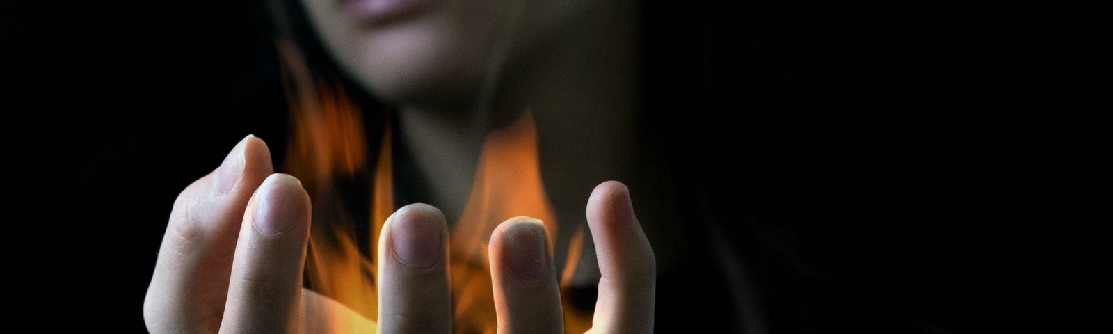 Woman in a black t shirt with arm out stretched and hands up, fire in the palm of her hand.