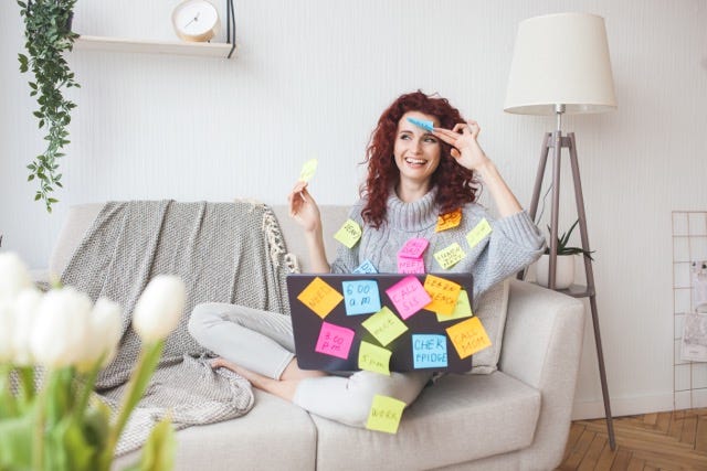 woman working at the laptop covered in sticky notes with all the tasks she needs to do