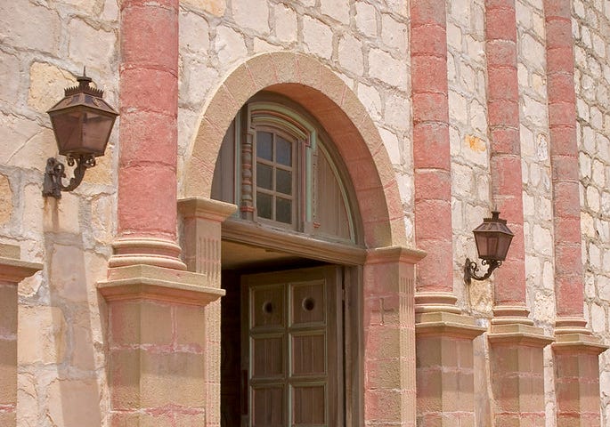 An open door in a pink limestone building.