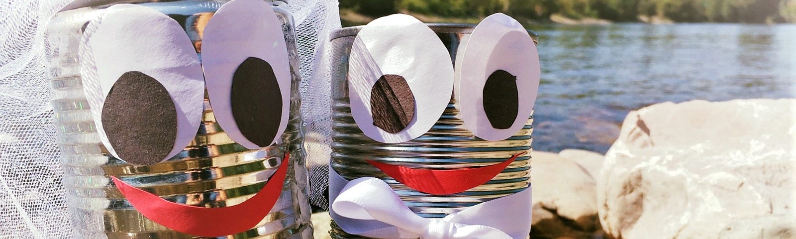 Two cans with cartoon faces are dressed up as a bride and groom.