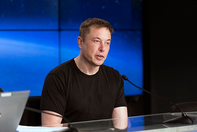 Elon Musk wearing a black shirt at a press conference.