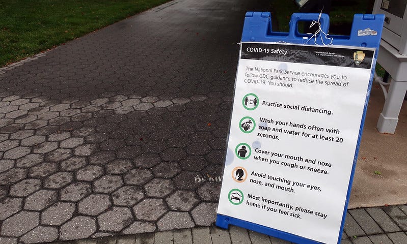 A sidewalk sign that details public health and safety guidelines for COVID-19.