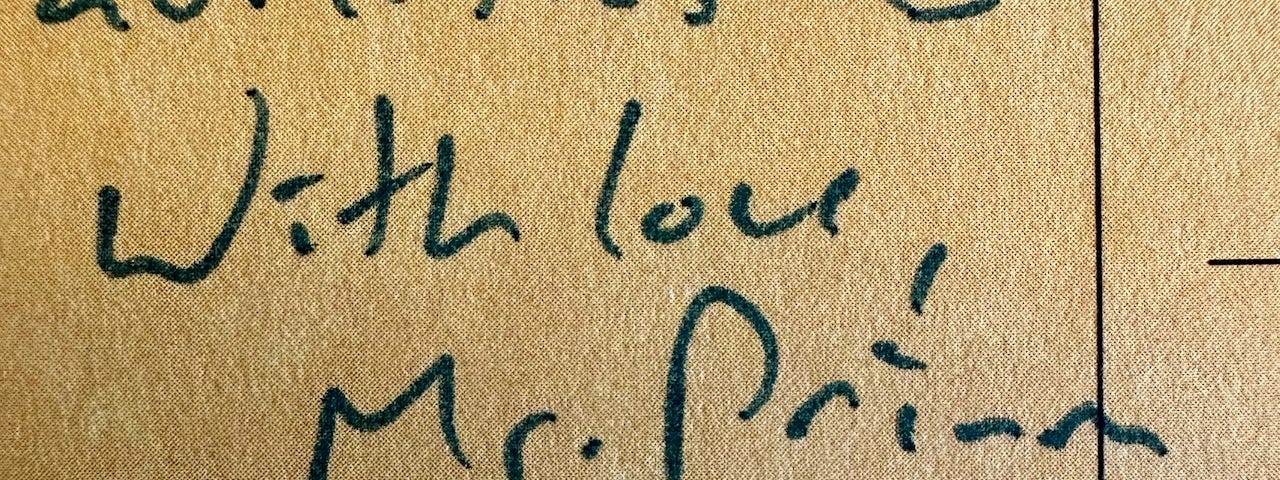 A macro image of a cardboard postcard. Handwritten text reads, “With love, Mr. Primm”.