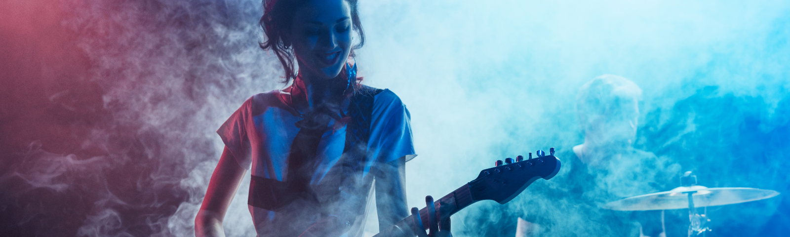Girl playing a guitar on a smokey stage.