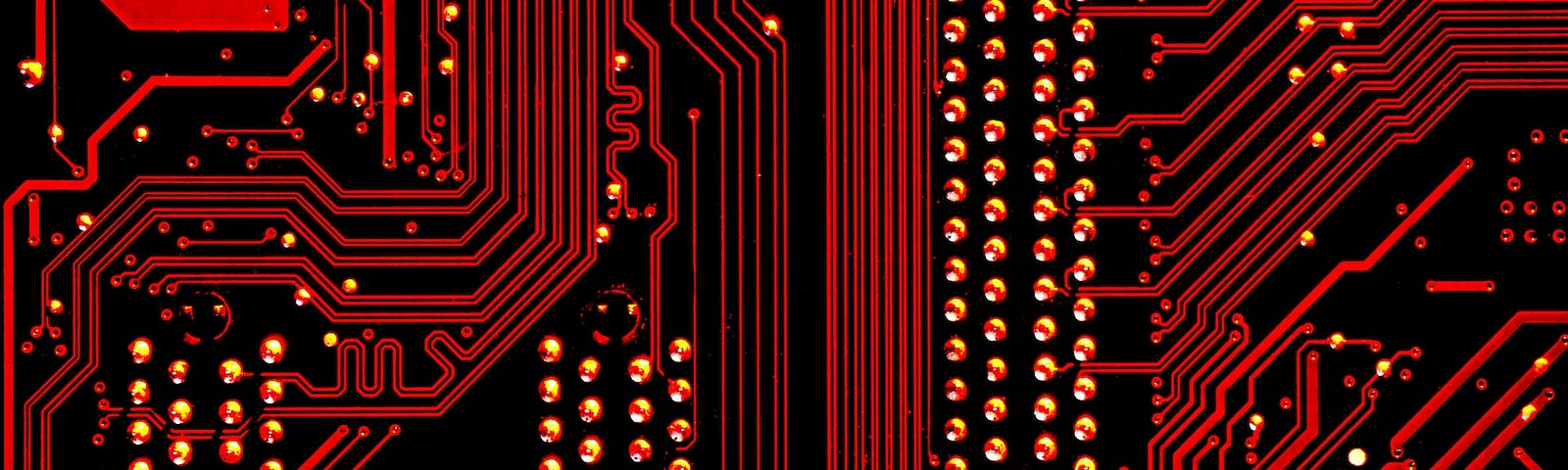 IMAGE: In red tones, the back of a electronic board showing the connections and the soldering