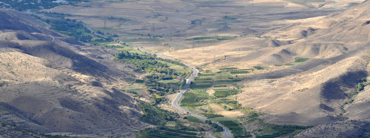 A road in a green valley surrounded by arid mountains.
