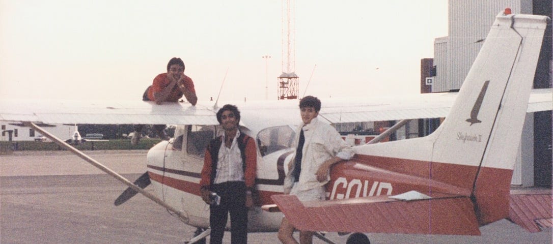 A red and white Cessna 172 with the author lying on a wing, posing with two friends who are standing on the ground by the plane.