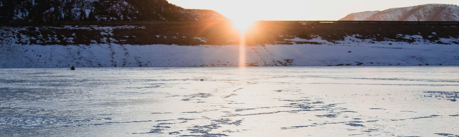 sun rising over hill in background, snow containing footprints in foreground