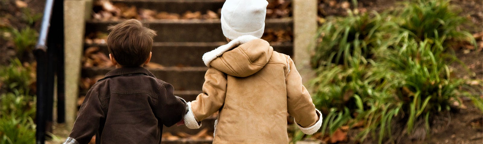 Back view of young boy and girl holding hands and walking toward staircase