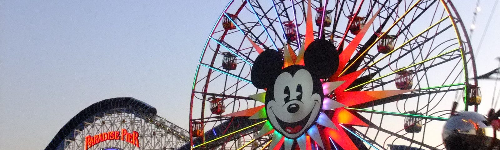 A giant Ferris wheel decorated with Mickey Mouse’s face. A rollercoaster is in the background.