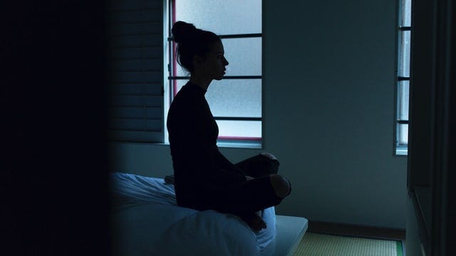 a gloomy room with a person sitting cross legged staring into oblivion.