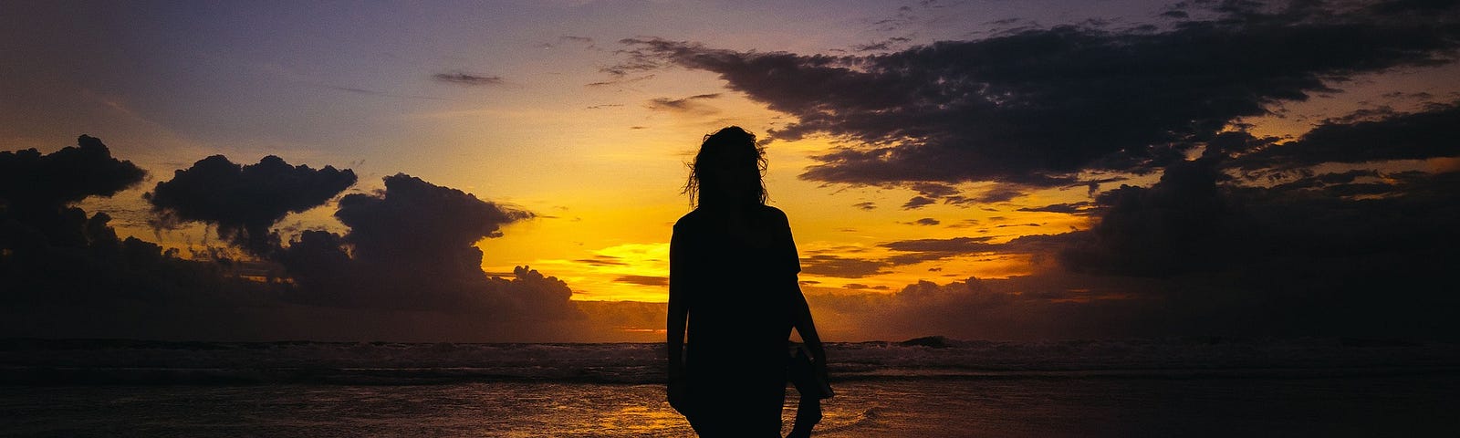 A silhouette of someone wading in shallow water with the sunset behind them.
