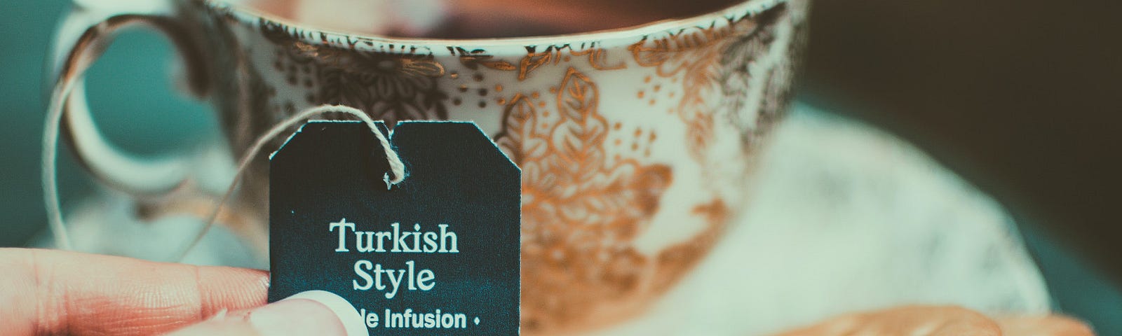 A cup of “Turkish Style” tea in a bone china teacup. Two Rich Tea biscuits rest on the saucer.