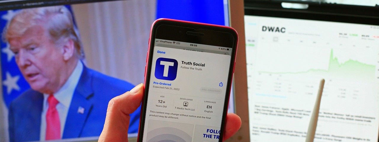 IMAGE: A smartphone with the Truth Social app installation screen, in front of a screen with an image of Donald Trump
