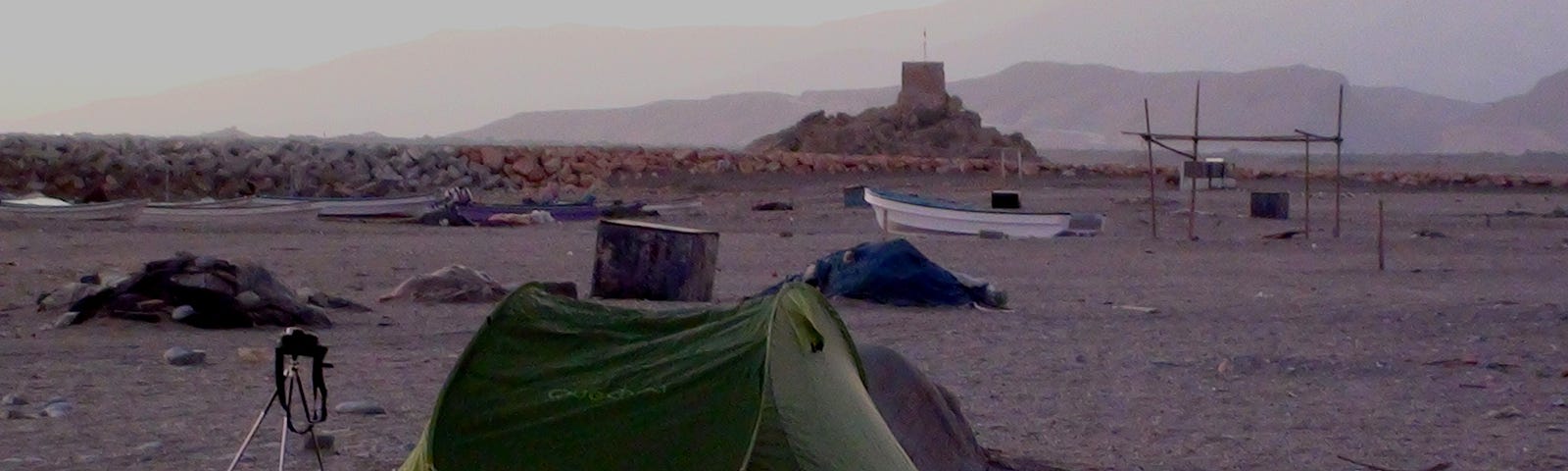 Bivouac at the beach of Qurayyat. A tripod with a film camera is standing next to the tent and waiting for the sunrise.