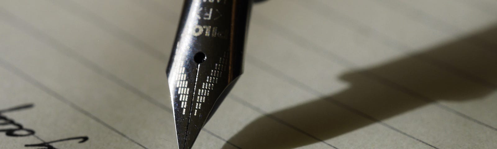 A close up photograph of a fountain pen mid-writing. A small amount of the handwriting can be see, although it is illegible and very cursive.
