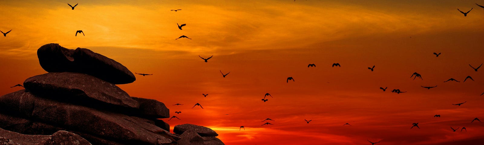 a stack of rocks set against a sunset with a flock of birds flying home to nest