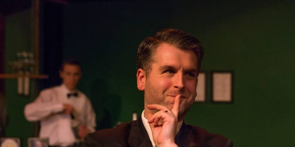 An actor (the author) on stage with finger to his pursed lips.