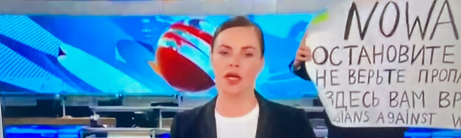 Editor-producer Marina Ovsyannikova holds protest sign behind female anchor on Russian state television news program on Channel One.