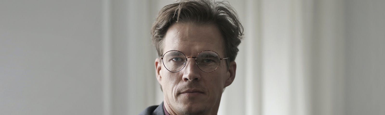 A mature man with glasses looks in front of a camera