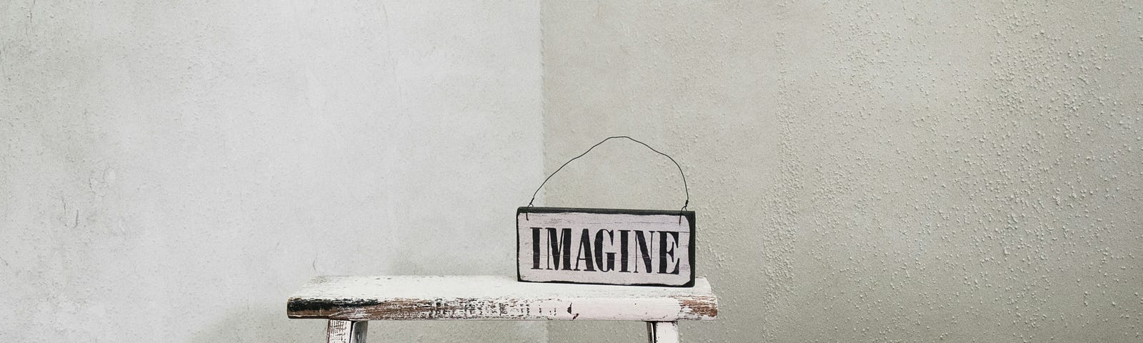 A white painted ladder has a sign on it that reads, “IMAGINE.”