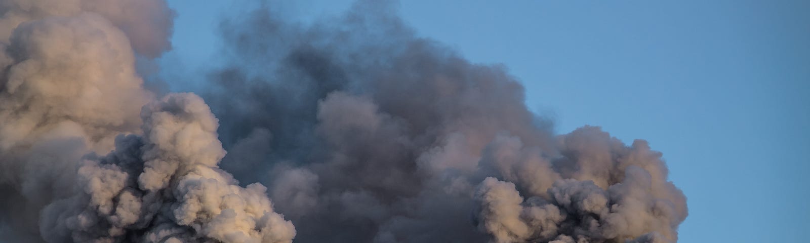 Two red and white smoke stacks releasing dark smoke into the air. Photo by kapichka/Adobe Stock