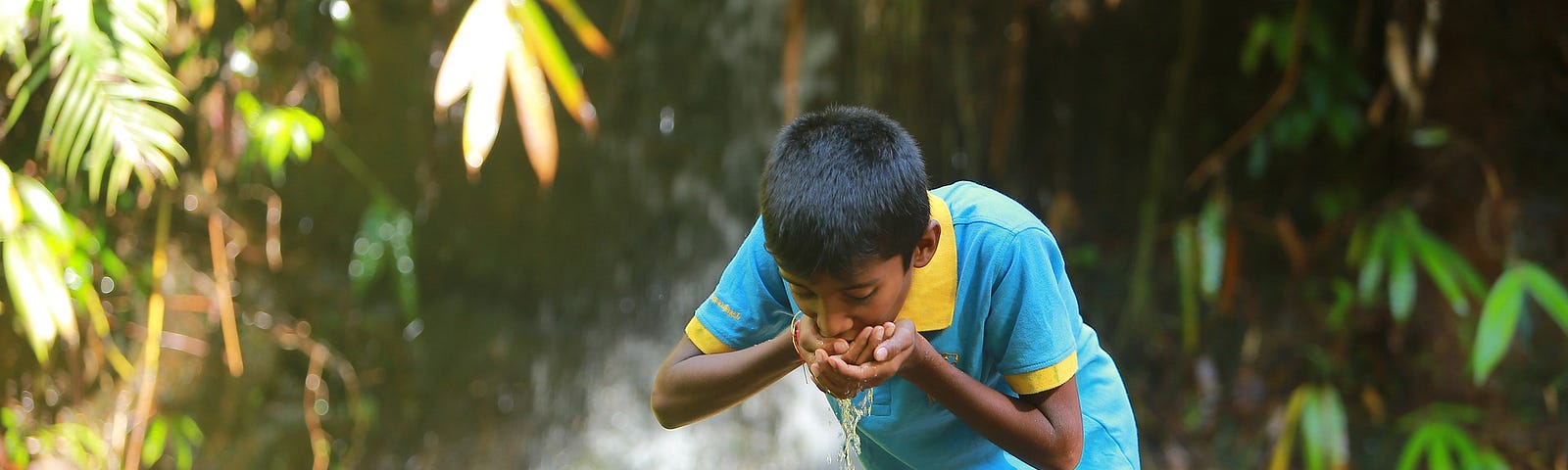 Indian boy blue clothing drinking water from an open pipe in a jungle