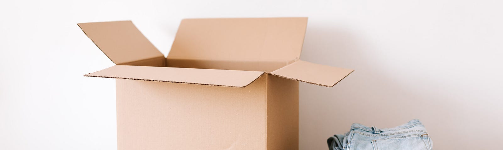 A moving box with packing tape, scissors, and clothes placed beside it on a table