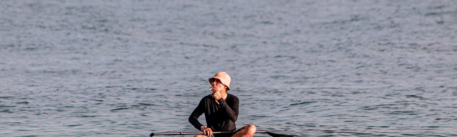 Man smoking a cigarette sitting on a paddle surf. The board floats in the sea.