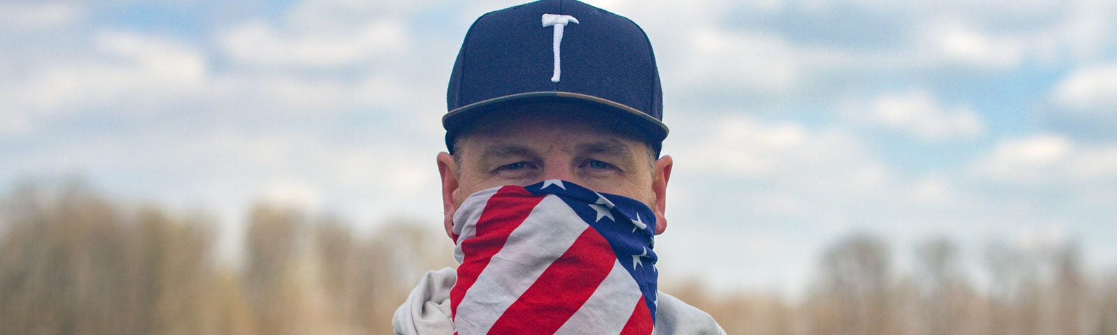 man in black hat with American flag bandana on face