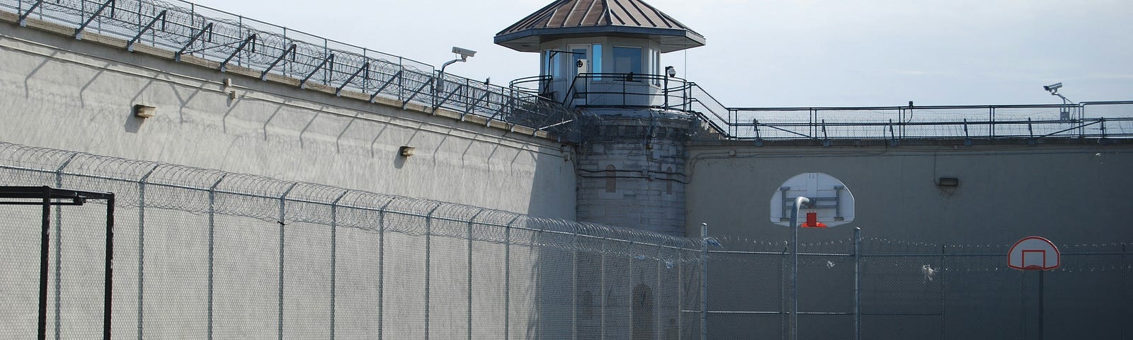 Picture of a prison yard, with fences and high walls that are covered by barbed wire.