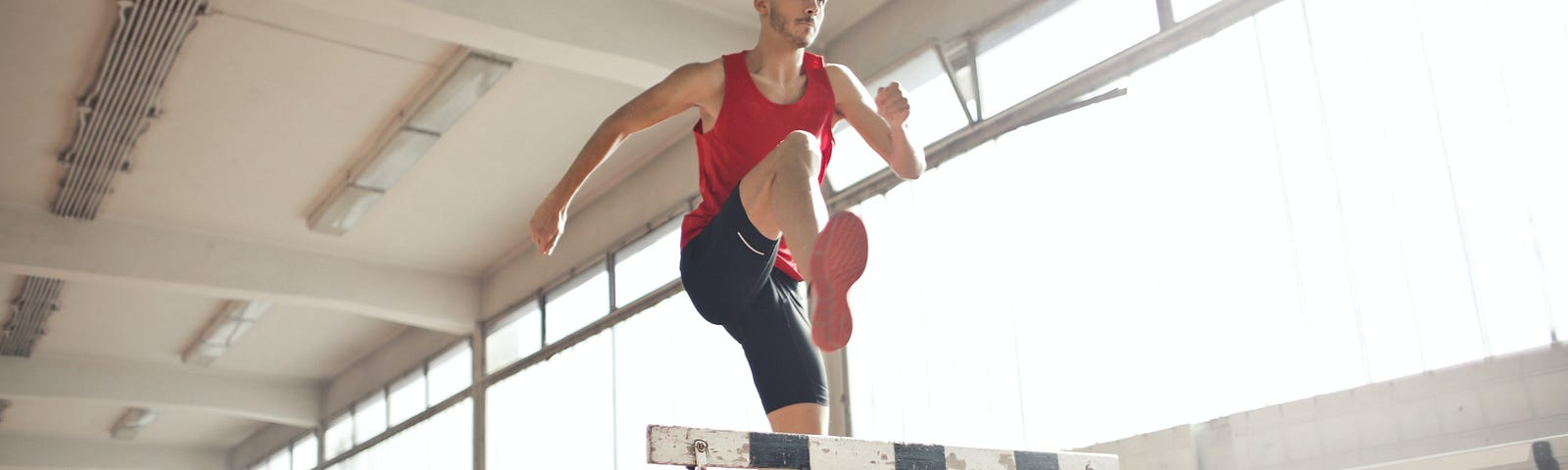 Athletic man jumping over hurdle