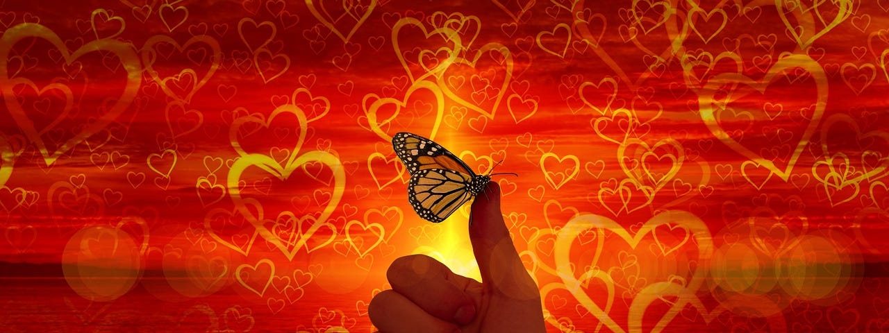 Against a backgroud red with yellow hearts, a butterfly perches on a person’s thumb.