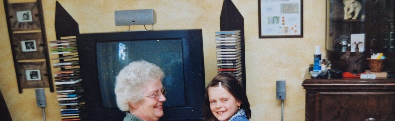 Family photo of the author as a young child sitting on her grandmother’s lap. Both are smiling at a table where a birthday cake with lit candles awaits.