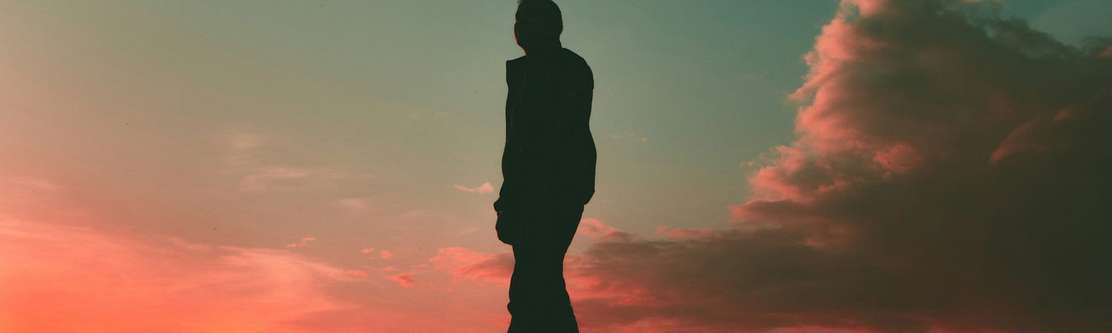 Silhouette of a man at sunset. Pink sky and clouds.