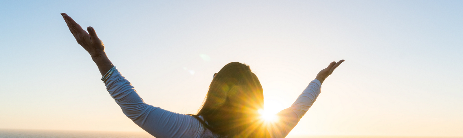 Woman raising up her arms to Heaven against the sunset